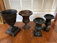 Four decorative urns on hardwood floor in front of white shuttered background showing the complete lot.