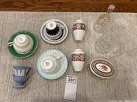 All items in the lot arranged on a beige textured rug; includes teacups, vases, covered dish, crystal bell, jam pot