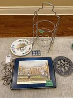 Overview photo showing the assembled 3-tier dessert stand, Aynsley cake plate with cake cutter, set of six metal card holders, boxed placemats, and decorative metal trivet arranged on floor.