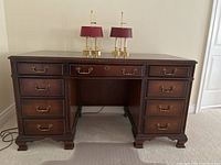 Front view of the double pedestal desk showing all 8 drawers and brass hardware, with two small lamps on top.