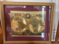 Frontal photo of gold foiled antique style world map replica in gold frame with maroon matte.