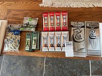 Lot arranged on floor with gloves in original packaging, several boxes of Titleist golf balls, and multiple packs of golf tees in front of a wooden floor.