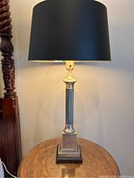 Full view of a lit antique silver-coloured table lamp with a black and gold shade on a wooden table.