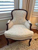 Front view of armchair showing carved wood frame and leaf patterned upholstery