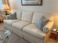 Front view of the sofa showing three-seat design, rolled arms, off-white upholstery, decorative pillows