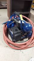 Full view of Campbell Hausfeld blue air compressor with coiled blue and red hoses attached.