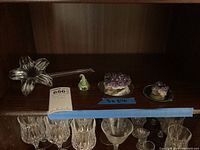 Two amethyst crystal clusters on round mirror display plates alongside a green glass Hershey Kiss sculpture and a clear lily-shaped glass vase on a dark wood shelf