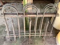 Front view of one iron fence panel showing arched top and fleur-de-lis finials