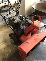 Front angled view of the orange Ariens snow blower with Tecumseh engine, showing tires, engine, and chute.