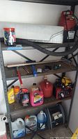Shelf holding various automotive care items lined up including mini vacuum, gas can, various bottles of fluids, battery charger, small red jump starter, and air compressor unit.