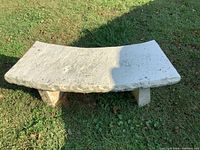 Front angle photo of a curved concrete bench piece on grass, showing weathered surface and flaking paint.