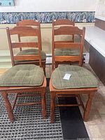 Four matching wooden dining chairs with ladder backs and greenish-gray cushions, placed on tile and vinyl flooring.
