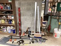 Shelf with red and white levels, drywall T-square, metal straight edge ruler, right angle ruler, some clamps and hand tools laid on floor, and assorted hardware containers on shelf.