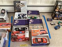 Overview of six collectible model racing cars in various packaging showing different brands and racing designs.