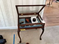 Front view of wood and glass display table with items inside under glass lid.