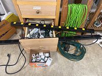 Two large black power strips with yellow outlet number labels, laying on the floor in front of wooden furniture with green and yellow extension cords coiled behind them.