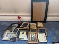 Overview of twenty assorted picture frames in various styles and sizes including one large black frame and several gold, silver, and wooden frames with decorative elements.