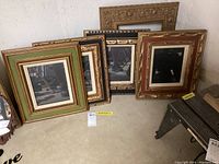 Wide view of all five picture frames leaning against wall showing various sizes and colors, some with glass and some without