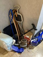 Multiple walking canes, a blue stool with cane feature, packages of briefs, and assorted health aids placed on floor against wall.