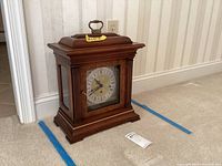 Full view of wooden mantel clock with brass handle on top, showing front and part of side.