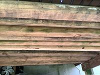 Photo showing 8 weathered wood timbers stacked horizontally with visible natural wood grain and signs of outdoor weathering.