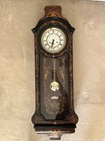 Front view of the tall regulator wall clock showing the wooden case with inlay, clock face with Roman numerals, and pendulum.