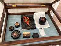 View of all six lacquer boxes arranged with the book in a glass display case, showing their relative sizes and designs.