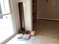 Photo showing the wooden plate shelf leaning against the wall next to the window, with the three ceramic plates, packaging, and paperwork arranged in front on carpet.