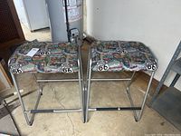 Two metal stools positioned side by side showing their metal tubular frames and patterned fabric seats.