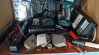 Wide shot of lot on wooden shelf displaying Makita drill with battery, charger, electrical tester with leads, plumb lines, hand tools, and lights.