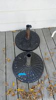Two black heavy base umbrella stands on wooden deck, showing overall design and wear