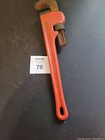 Photo of an 18 inch pipe wrench with an orange-red handle against a dark surface background.