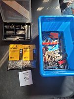 View of black plastic compartment case with assorted drill and screwdriver bits and two unopened DeWalt #2 drywall bit packages. Blue bin with loose bits in background.