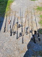 Full view of 9 fishing rods with reels laid on the ground showing various handles and reel types.