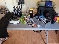 Photo showing all items on table including jars of nails, toolbags, snow pants, Coors Light bottles, and metal box with hardware.