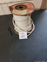 Photo of a nearly full roll of white house wiring on a rusty metal spool placed on a black surface next to a pen and auction lot tag