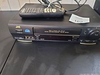 Front view of JVC Pro-Cyron HR-AU VCR with remote on top showing AV input jacks and control buttons.