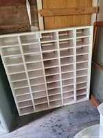 Front view of painted white cubby unit showing multiple rows and columns of storage compartments against a wooden wall.