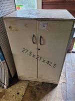 Front view of large metal storage cupboard with closed double doors and visible wear and scratches. Dimensions 27.5 x 21 x 42.5 inches shown on front.
