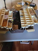 Full view of large vintage fishing tackle box opened, showing two fold-out trays with compartments, some fishing tackle bits inside, three drawers below