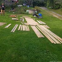 Photo showing wide variety of lumber pieces spread on grass with visible sorting by size and length.