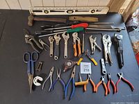 Photo showing the entire collection of vintage hand tools arranged neatly on a black surface. Includes a level, hammers, screwdrivers, various wrenches, pliers, tin snips, and scissors, with colorful handles in orange, blue, green, and red.