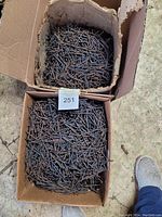 Two opened cardboard boxes filled with rusted 2 1/2 inch Ardox nails on a concrete surface.