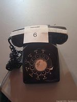 Top-down view of black rotary dial phone showing dial pad with numbers and letters and coiled cord attached to handset.