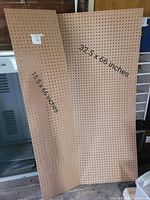Photo showing two brown pegboard panels leaning against a wall with size labels visible: 19.5 x 60 inches and 32.5 x 60 inches.