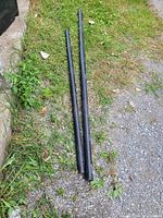 Two black PVC pipes lying on grass and gravel ground, showing possible sizes around 6 feet and 41 inches.