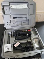 Black Roto Zip Rebel Spiral Saw tool in gray molded plastic carrying case with spare bits and manuals.