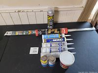 Full view of the sealant tubes, Flex Seal spray, metal stirring stick, and wood filler on black table.