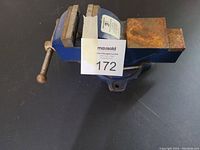 Front angle view of blue small vise with clamping handle and rust on flat jaws.