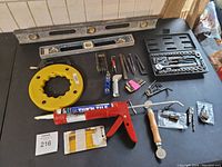 Photo showing the socket set with ratchet, two spirit levels, yellow wire puller, red grease gun, allen keys, screwdriver bits, utility knife and other assorted small hand tools